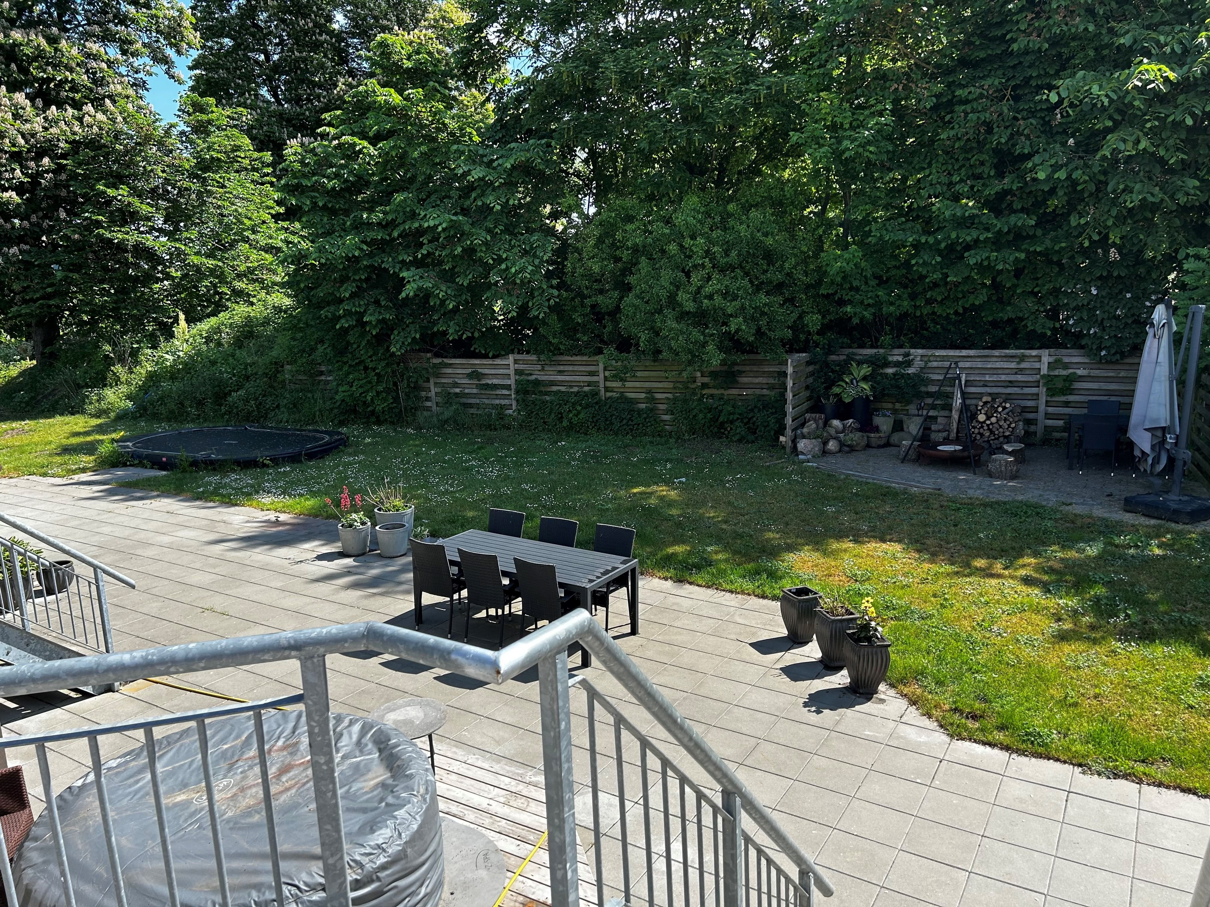 Terrasse med bord, stole og jacuzzi samt trætrappe og trampoline i baggrunden