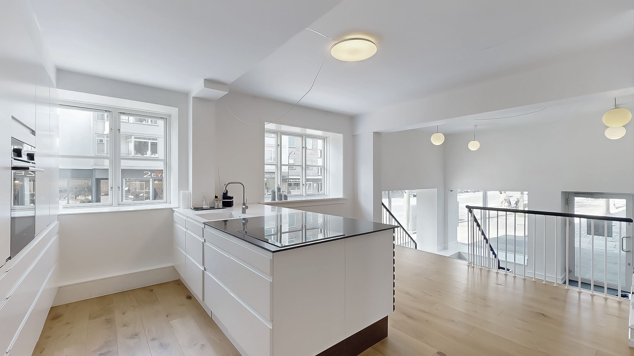 Hvidt kontorlokal med glasvinduer og moderne køkken med stolpelampe og hængelampe på loftet