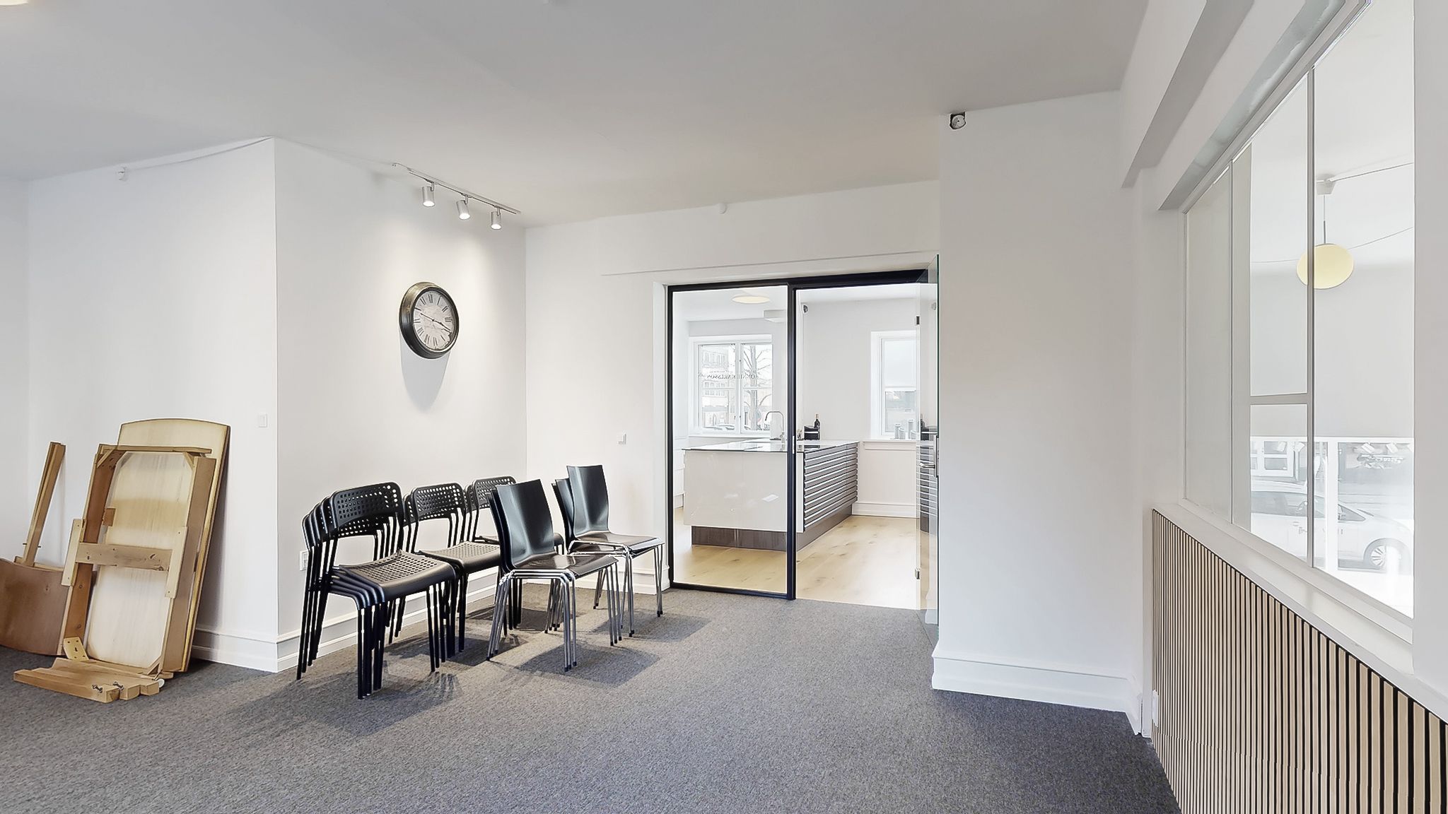 To rækker stolpeformede stole i stribet sort står på gulvet i et tomt kontorlokale med hvide vægge og møbler samt en åben