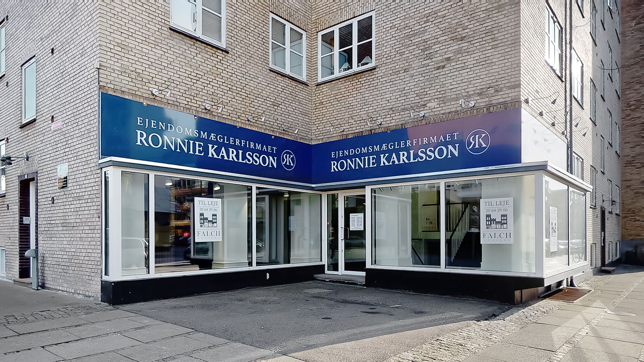 En forretningsbygning med et skilt, der læser "Ejendomsmæglerfirmaet Ronnie Karlsson" og logoet "RK". Der er vinduer med