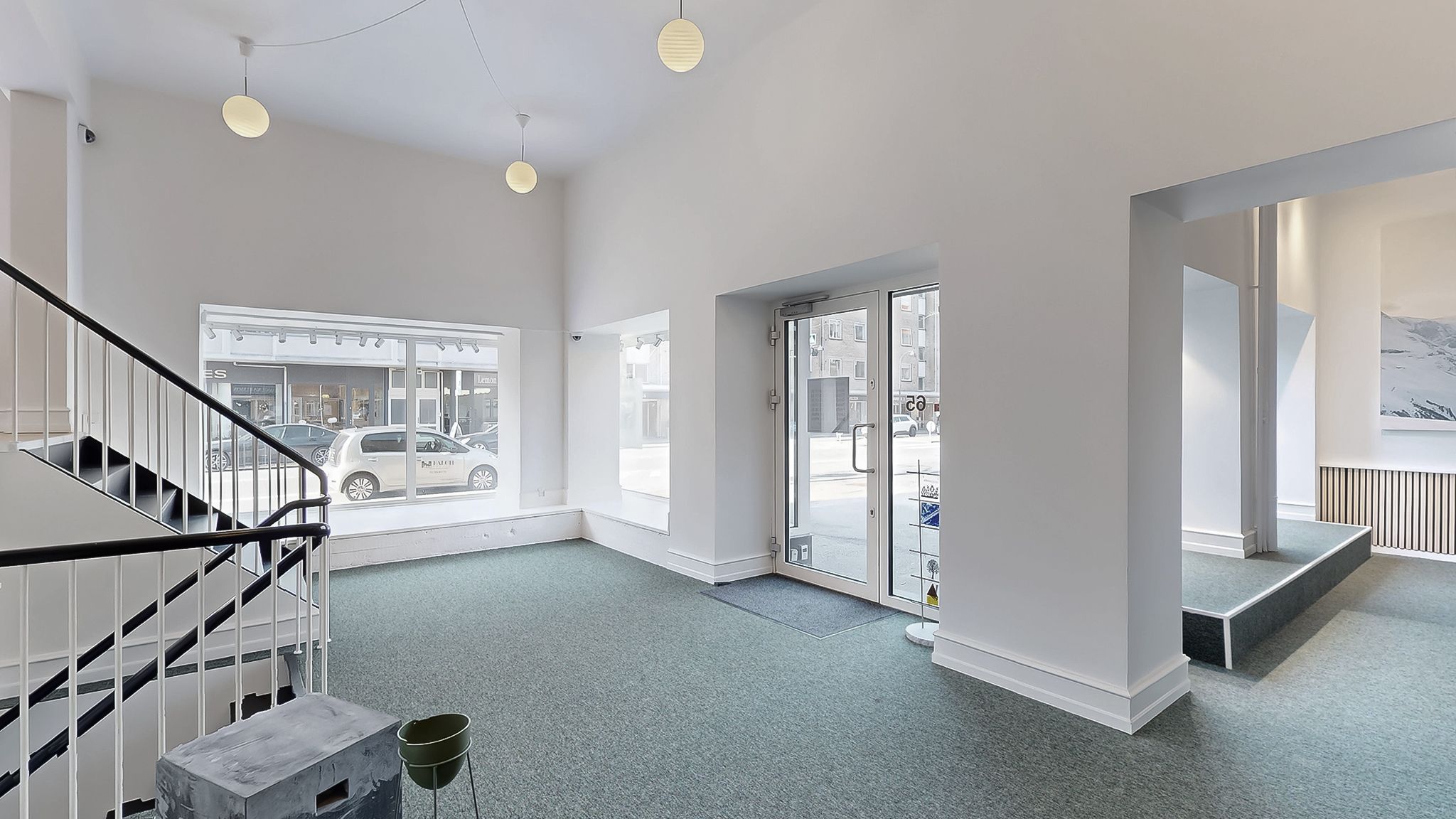 Kontor med lyst interiør, hvid gulvbelægning og glasdøre. Tre hængelampe på loftet og en indgangsdør med trægulv.