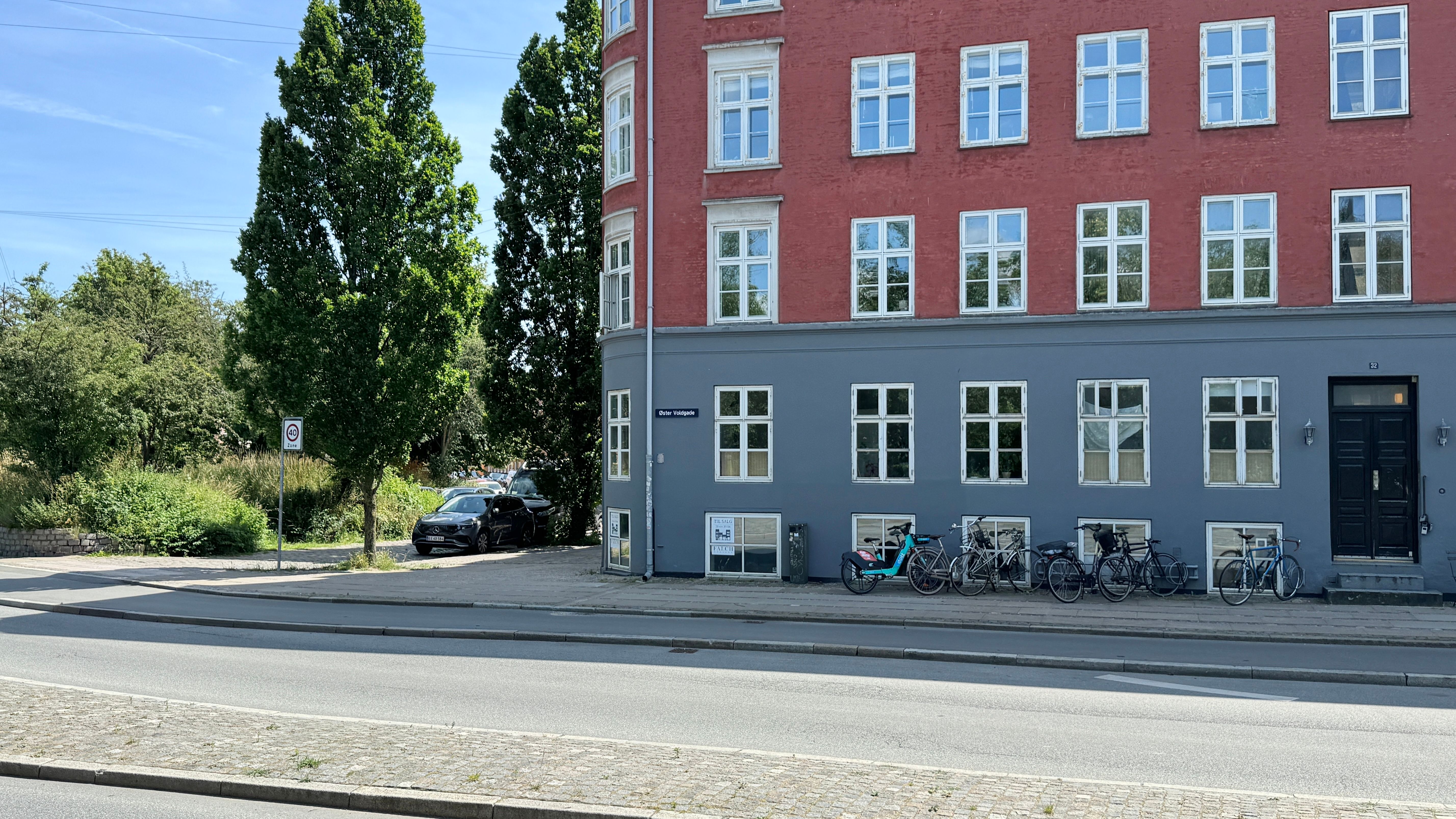 Parkeret bil ved en rødmalet lejlighedsbygning med flere cykler parkeret udenfor og et skilt med et køretøjsforbud