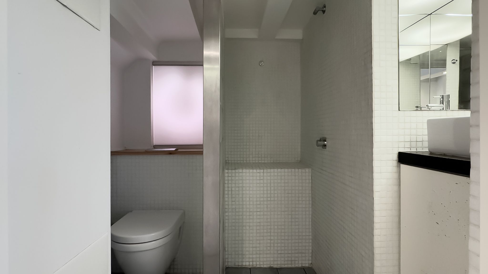 En hvidt badeværelse med hvid toilet, hvid spejl og hvid sæbehylde