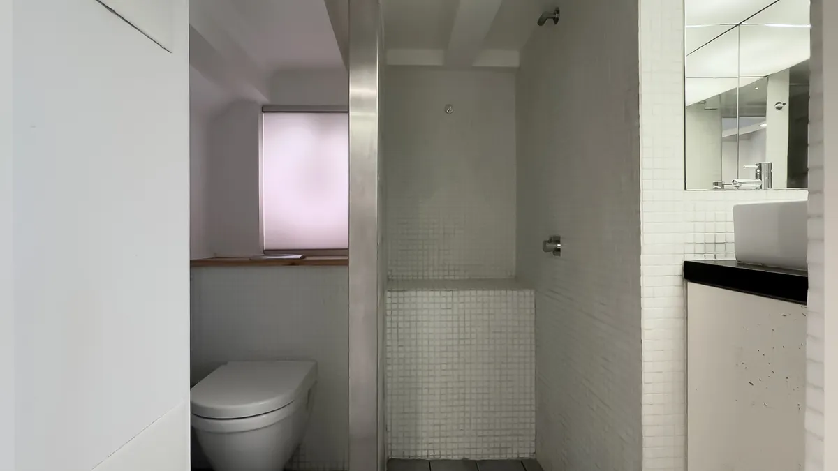 En hvidt badeværelse med hvid toilet, hvid spejl og hvid sæbehylde