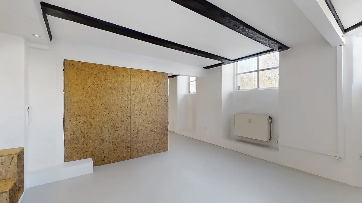 Et rum med hvide vægge, loft og gulv, to vinduer og en stor, brun dør lavet af spånplade