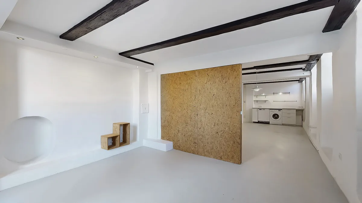 Minimalistisk stue med hvide vægge, lysegul gulv og lysekroner. Møbler og apparater er ikke synlige på billedet.