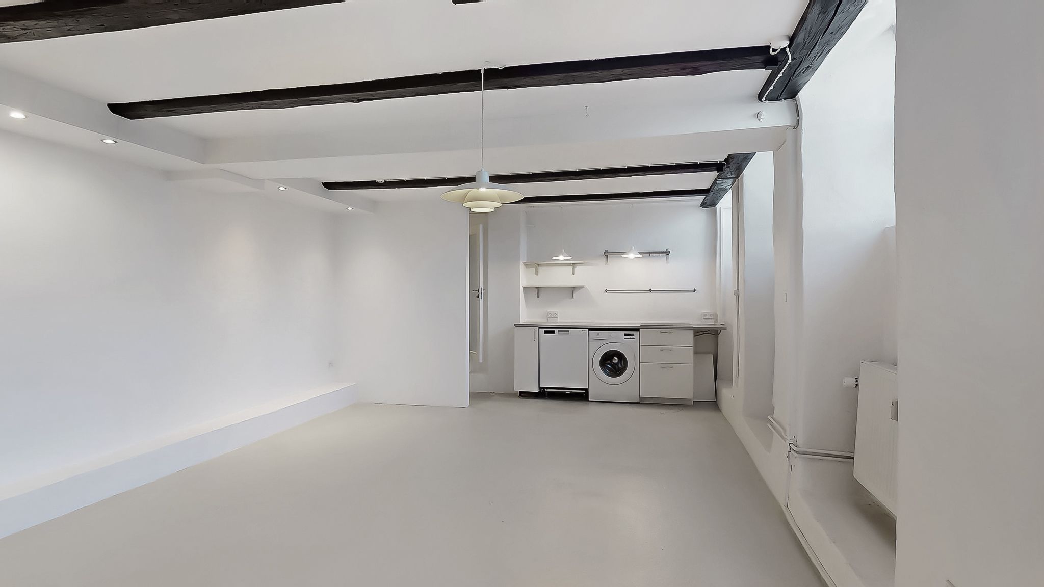 Rent og moderne værelse med hvide vægge og loft. Møblerne er enkelt og minimalistisk designet. En vaskemaskine står i
