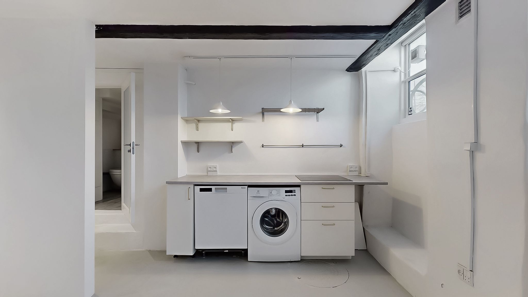 Et moderne badeværelse med hvidt loft og vægge, lyse pendularlampe, hvidt vaskemaskine og opvaskemaskine samt to hængehylder