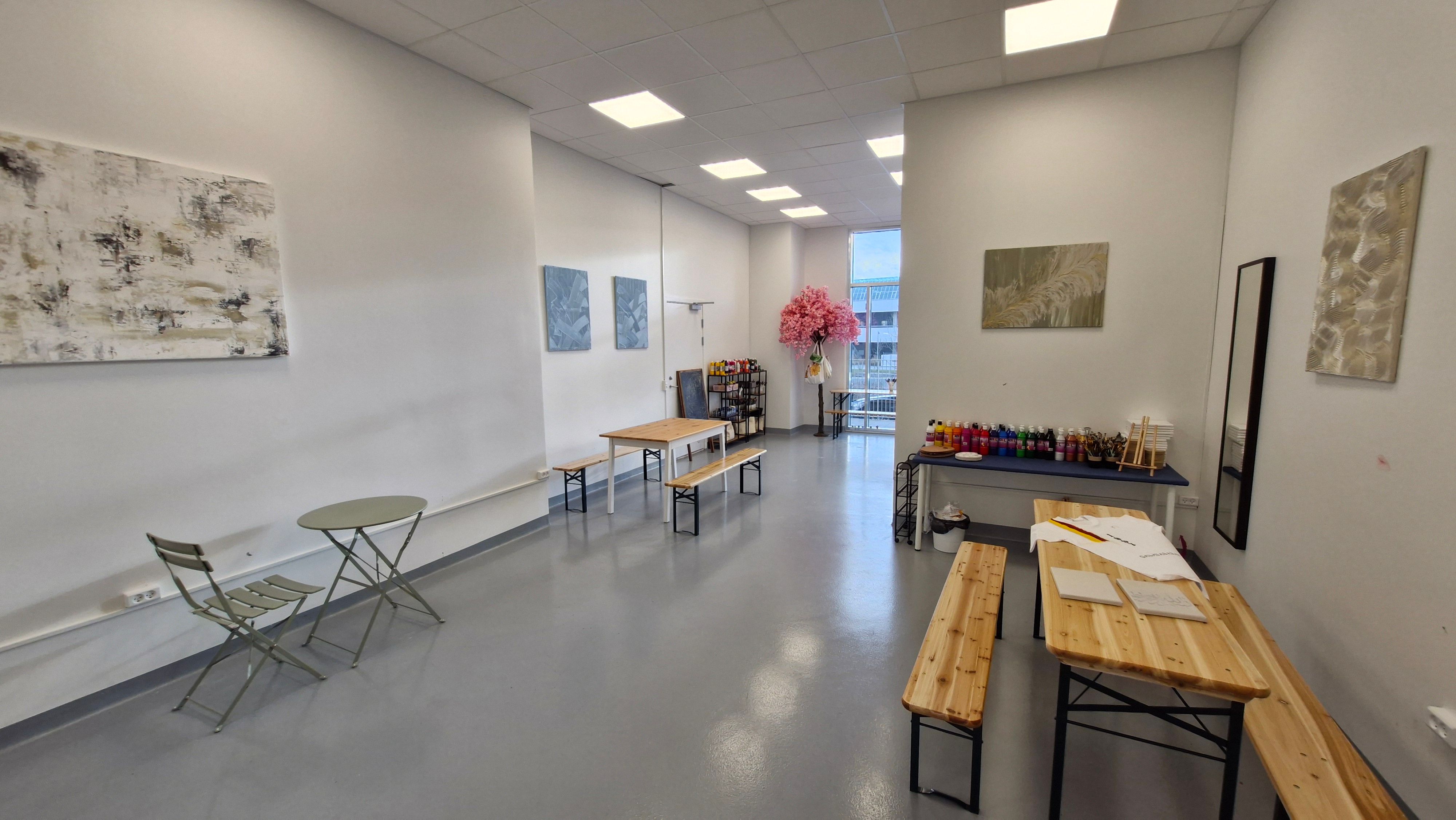 Kunstværker hænger på væggene, og flere stole og bænke er placeret. Der er flere bønner på gulvet. På et bord er der nogle