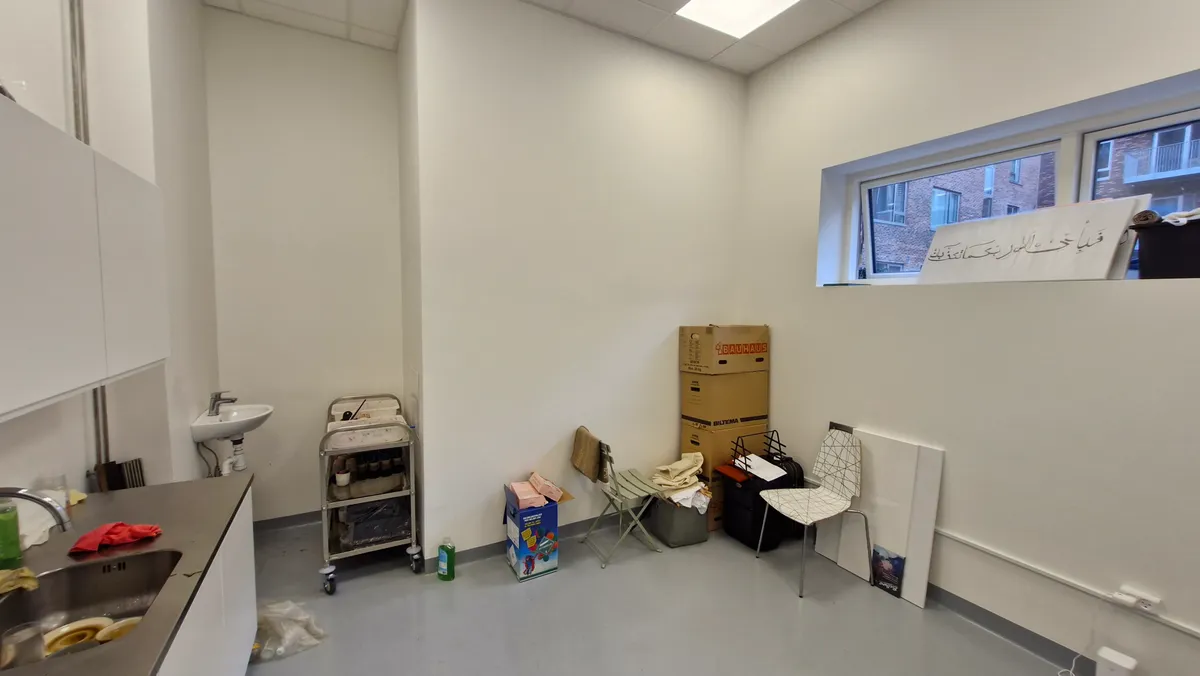 Et tomt rum med hvide vægge, vinduer, skraldespand, toilet, håndvask, køkkenbord, stålampe, hængekøkken og flere bokse og