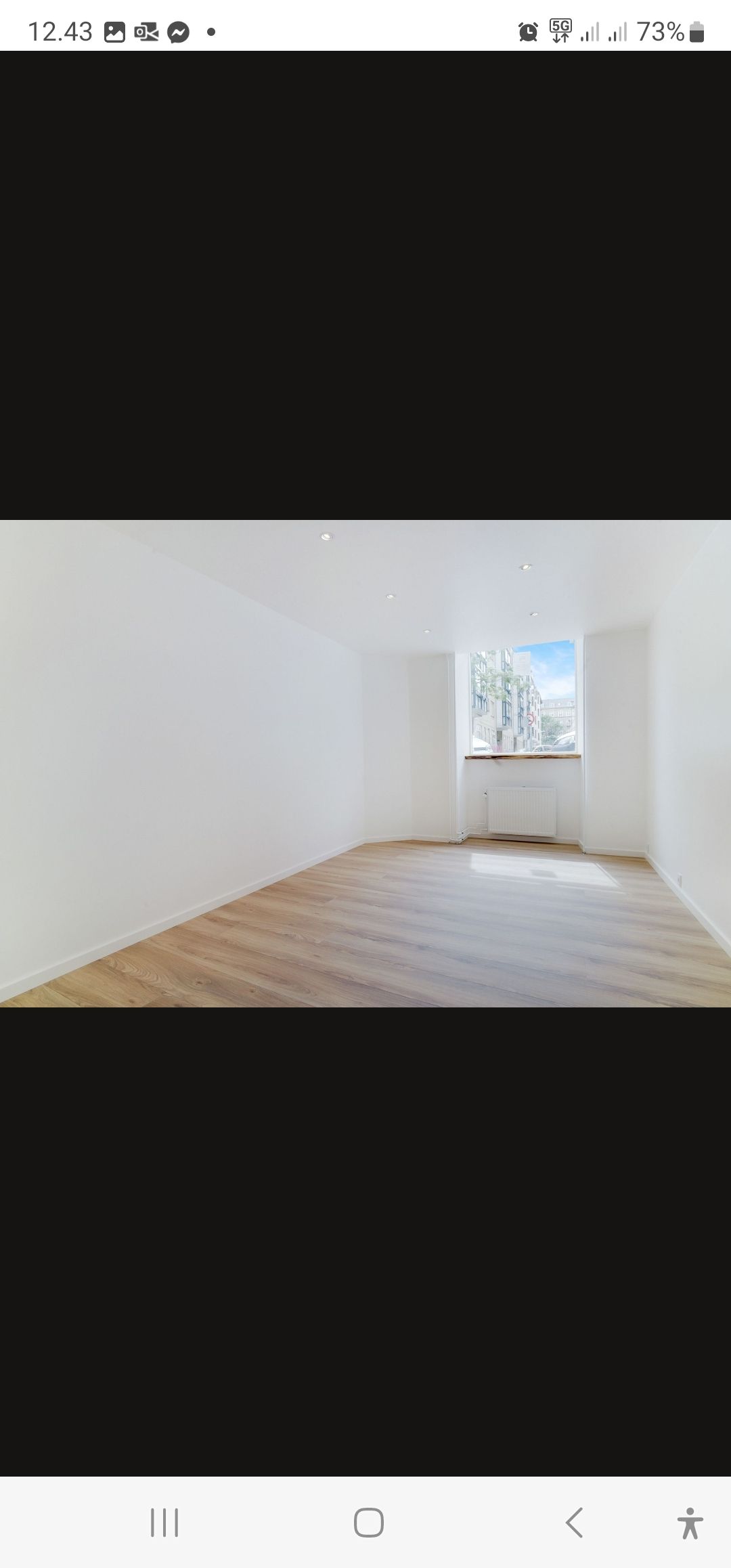 en tom stue med lysegult gulv og hvide vægge samt et vindue med udsigt til bygninger udenfor