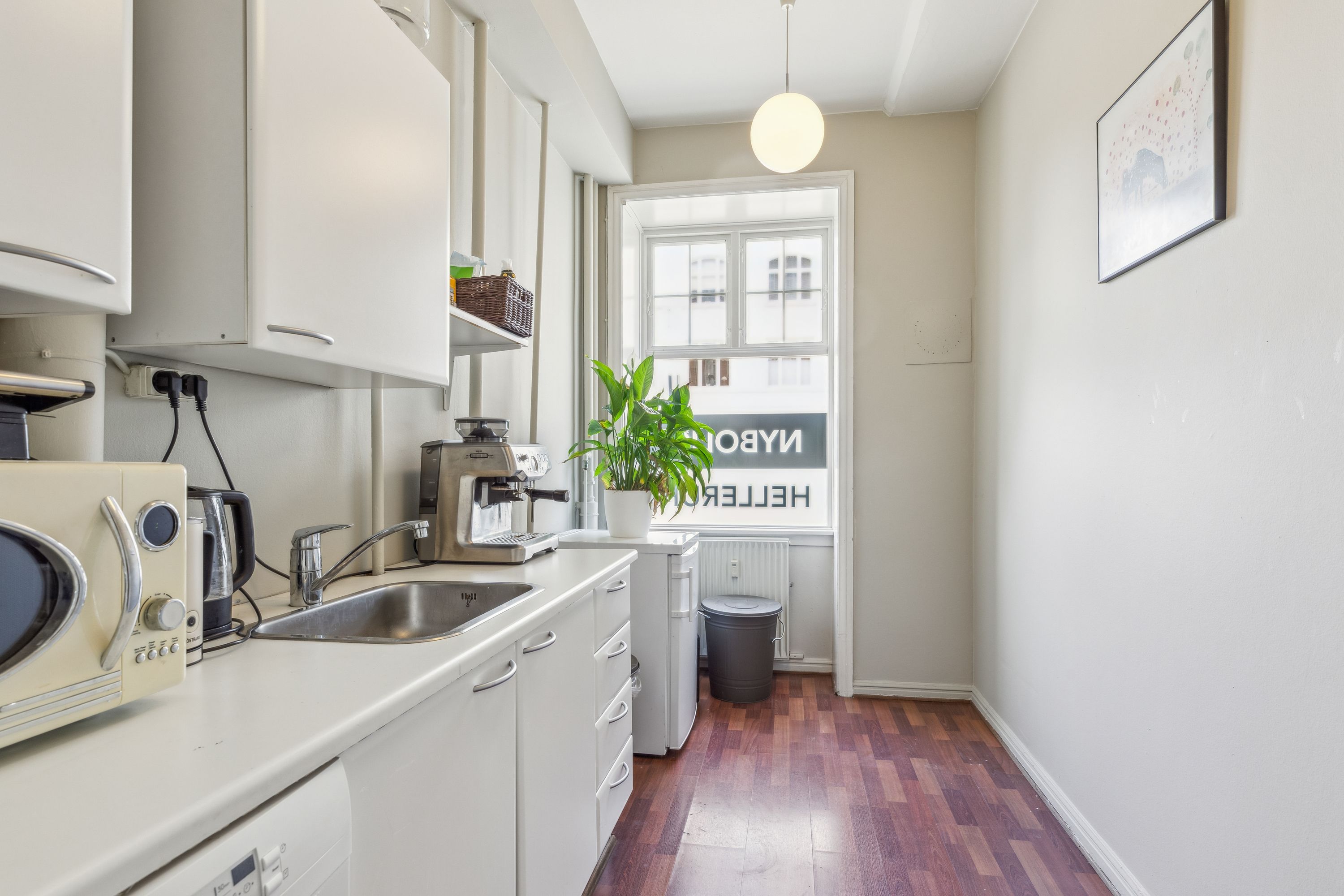 Lejlighed med hvidt køkken og højloft. Moderne køkken med kedel, kaffemaskine, mikrobølgeovn og lyse puder. Vindue med