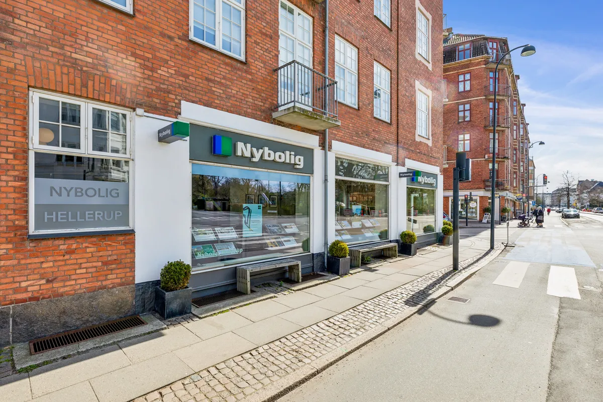 Nybolig-kontor i Hellerup med stolpe og grønne plantekasser på fortovet, nybolig-skilt og glasvinduer med reklamemateriale