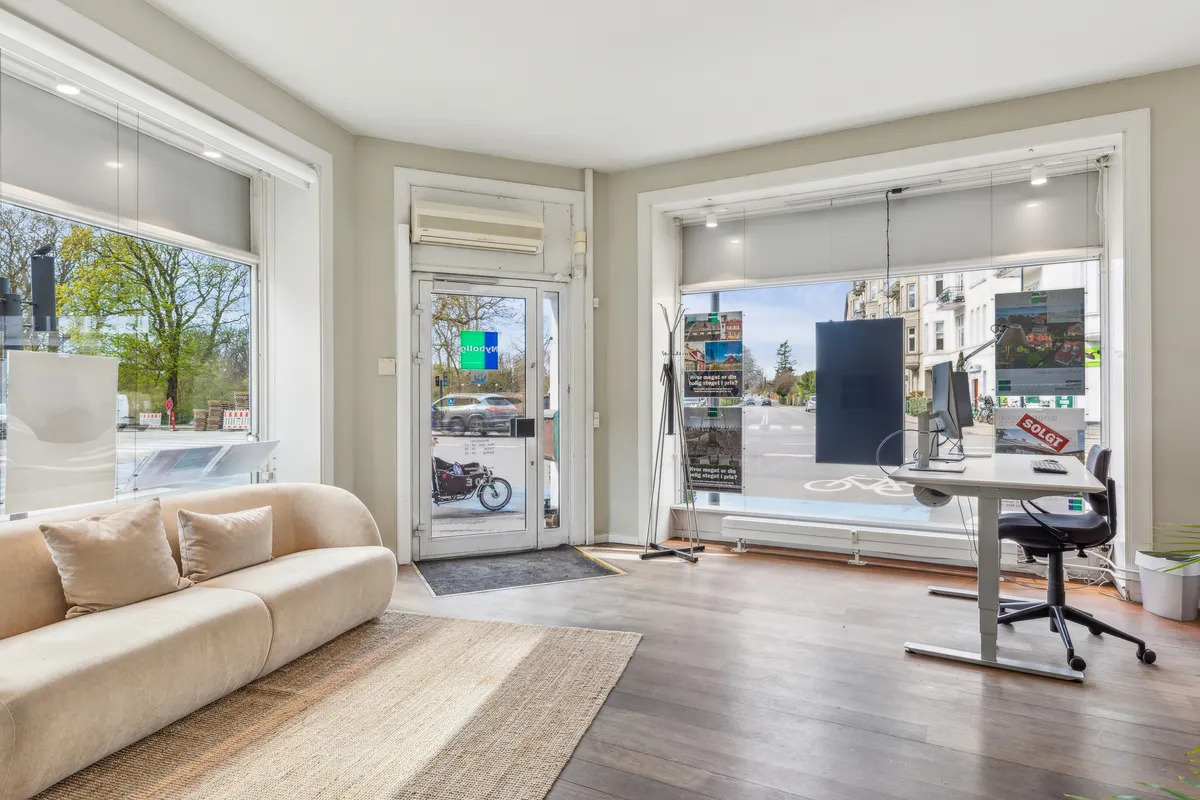 Nydelig indgangszone med behagelig sofa, skrivebord og lyse vinduer med udsigt til gaden og en bygning med kørende biler