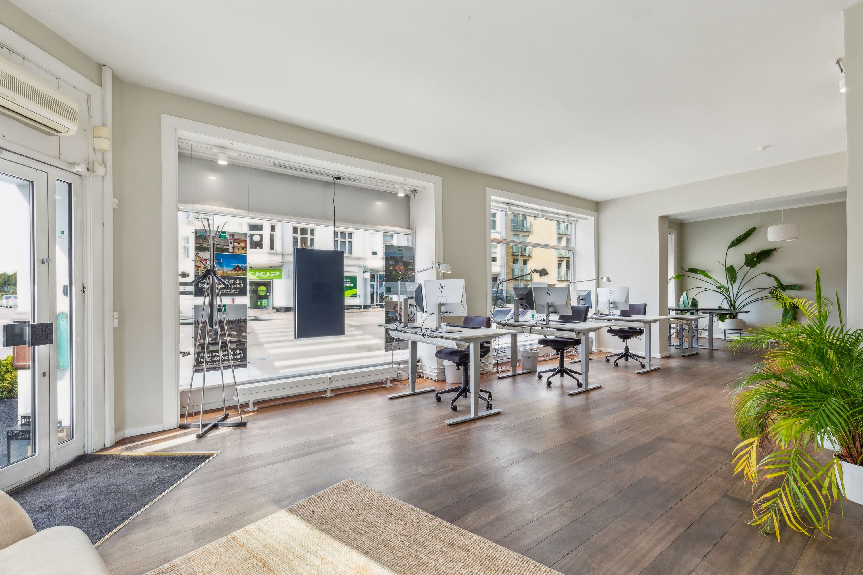 Moderne kontor med højt til loftet, vinduer med gardiner, trægulv, skriveborde med computere, stole og lysekroner.