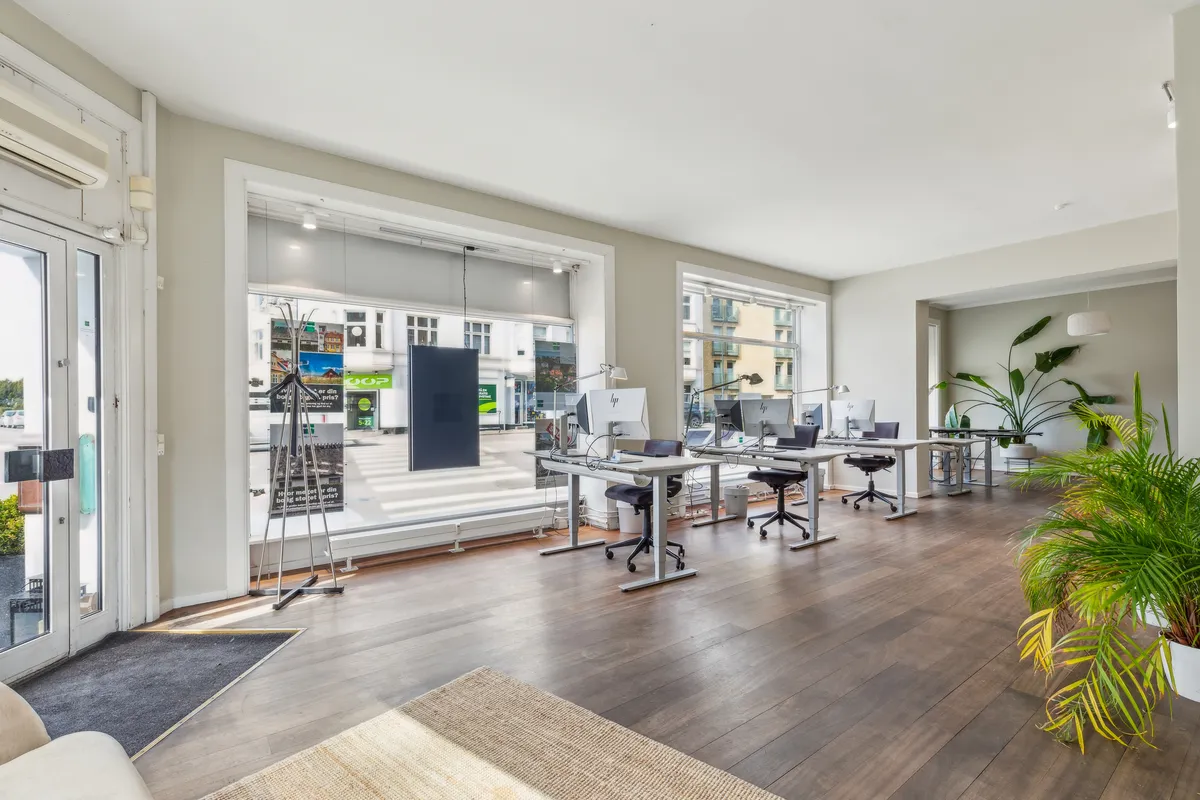 Moderne kontor med højt til loftet, vinduer med gardiner, trægulv, skriveborde med computere, stole og lysekroner.