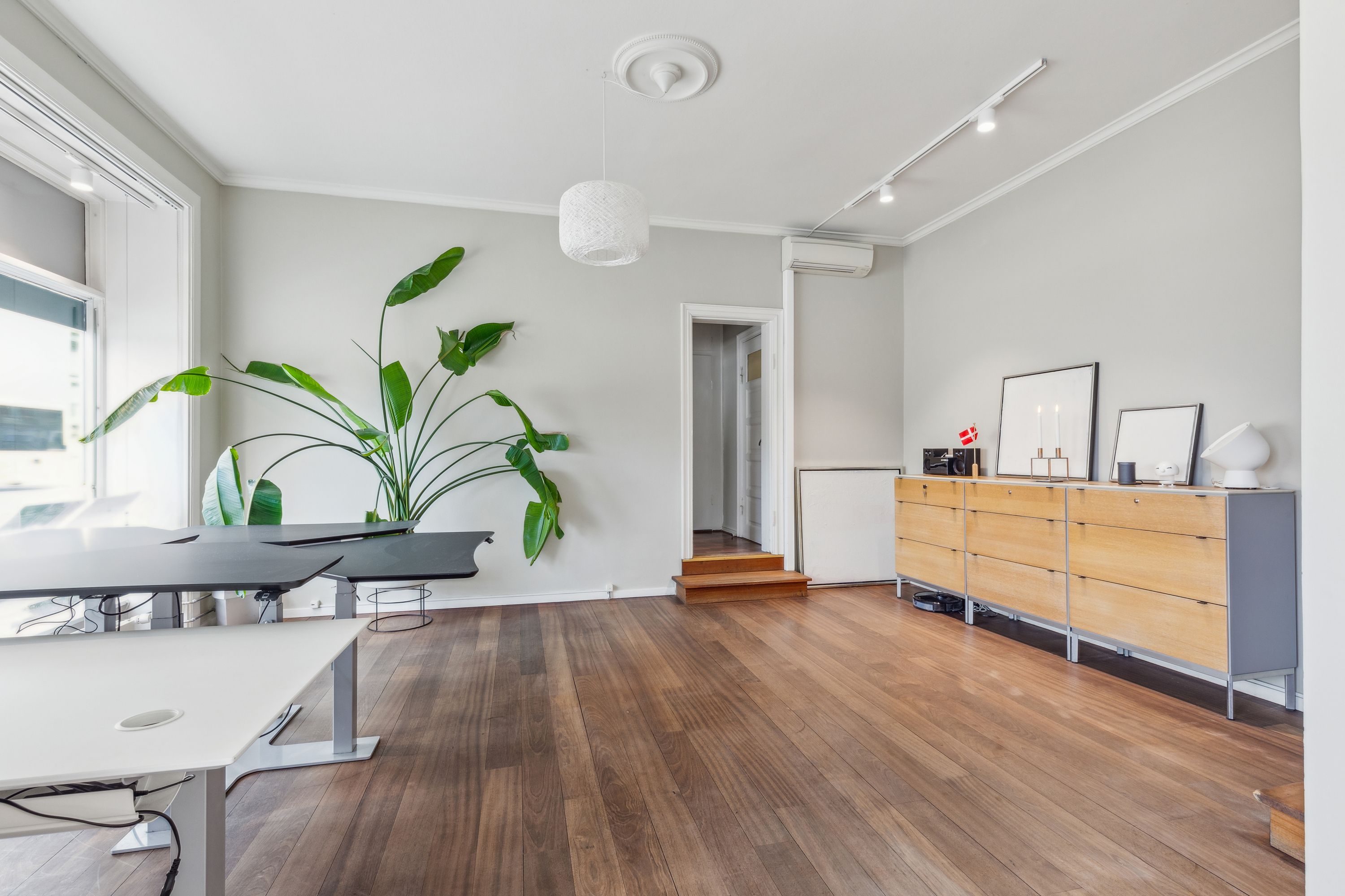 Erhvervsandel med møbelsæt, højt loft, højt vindue, plante og lysekroner.