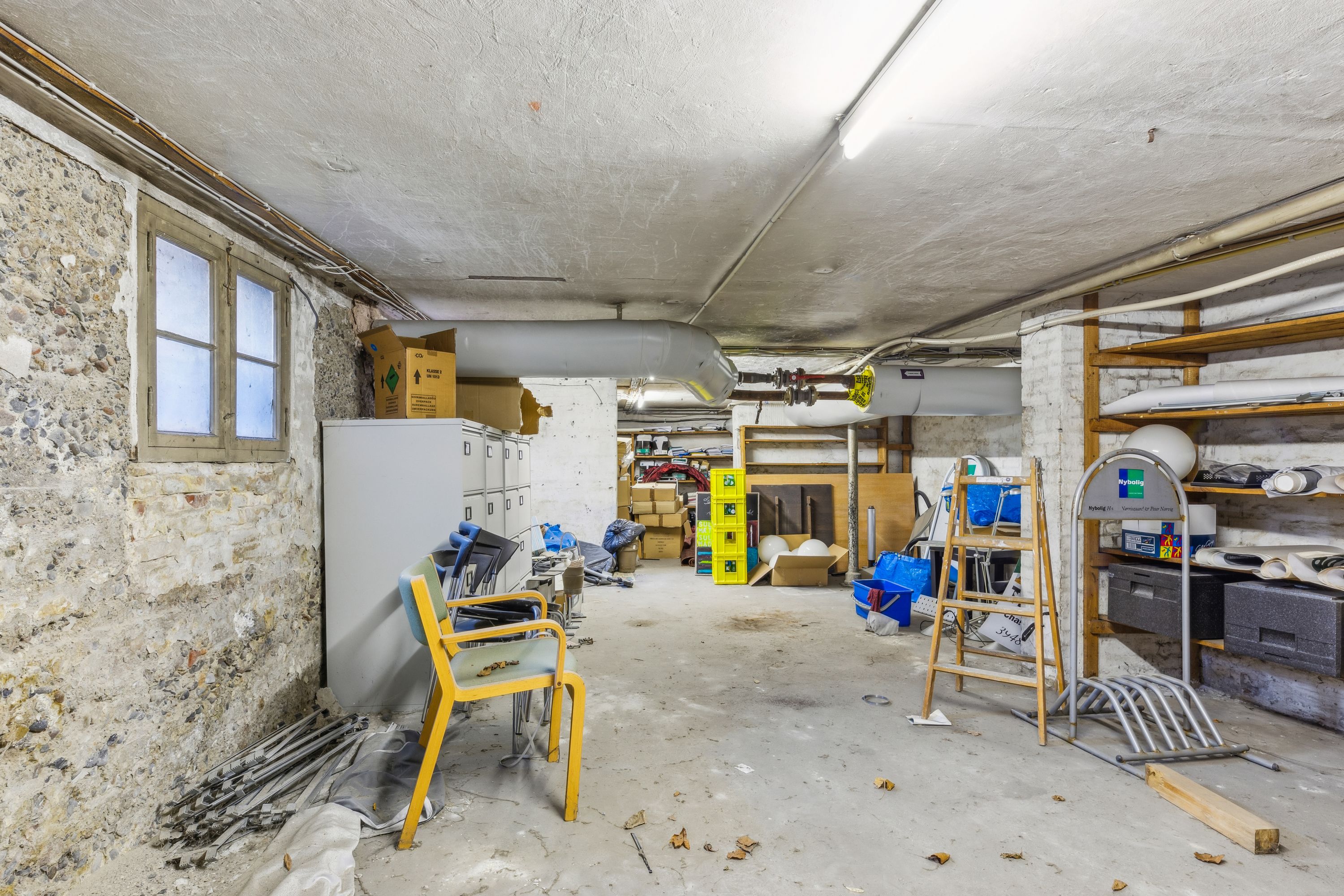 Lagerrum med to stole, flere kufferter, rør og tøjkasse i det lyse rum med vindue og vægge af sten
