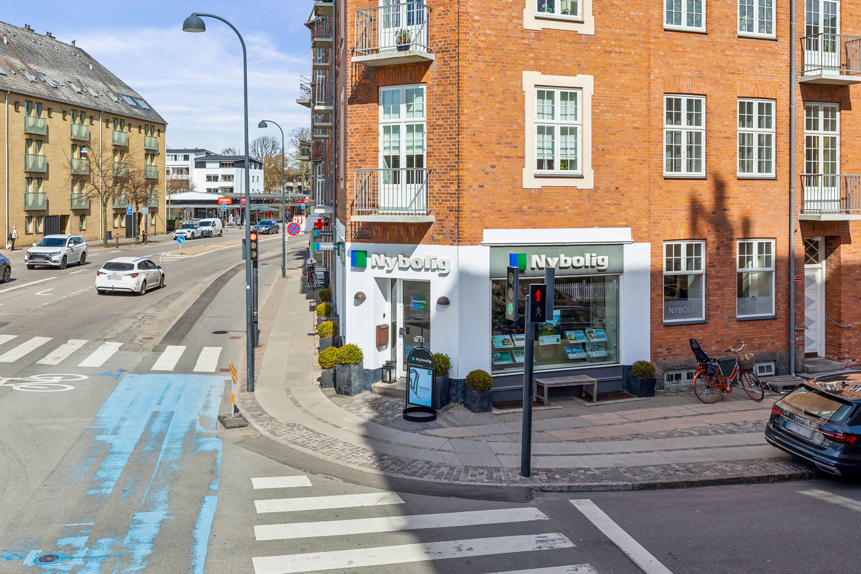 En bilforhandler i Nyboelig ligger på hjørnet af Strandvejen og Strandvejen 130E. Der er en ny bilparkeret på fortovet.