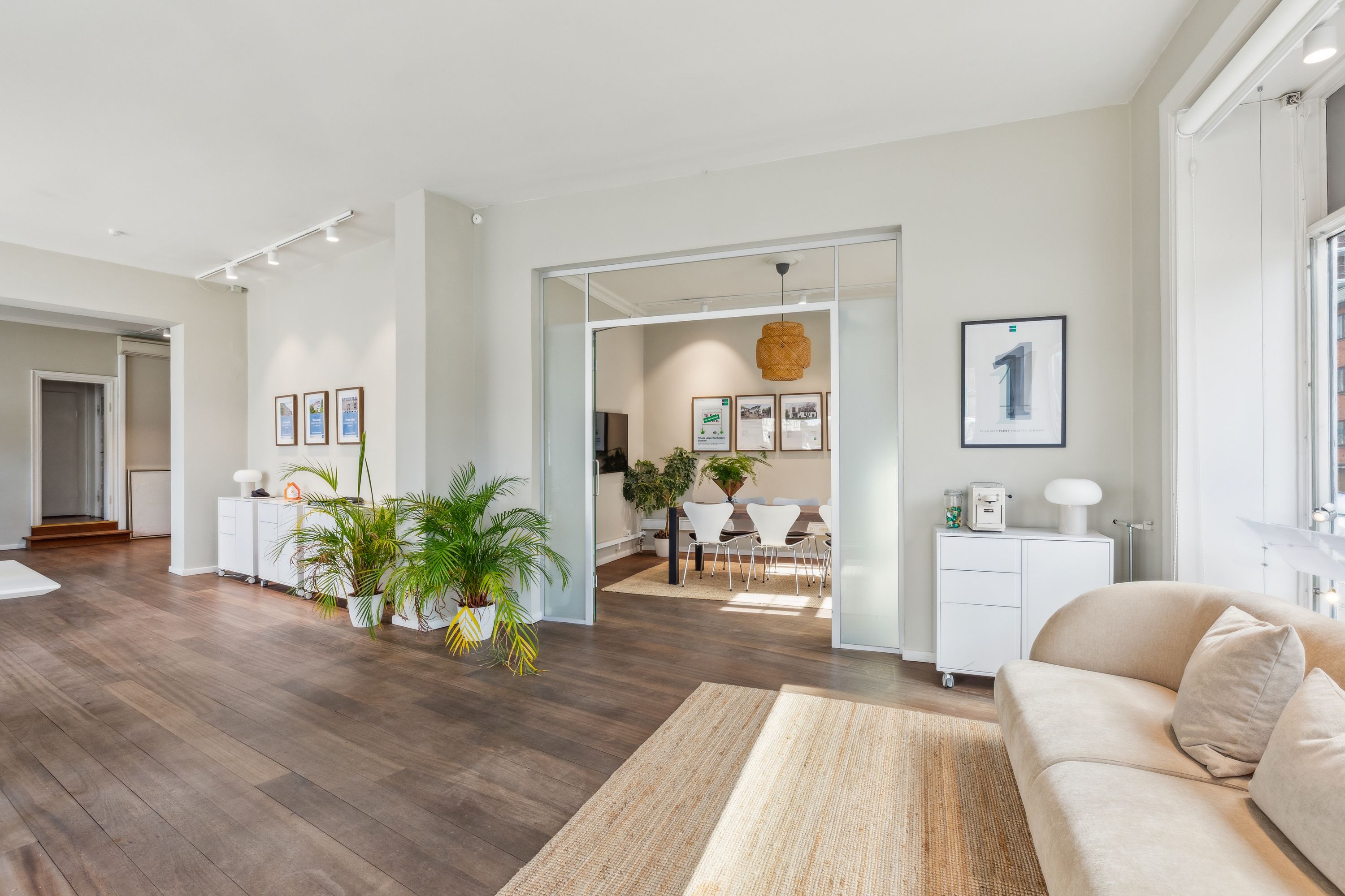 Et velmøbleret og moderne stue med højt til loftet, hvide vægge, lyse trægulve, store vinduer og indbydende møbler og