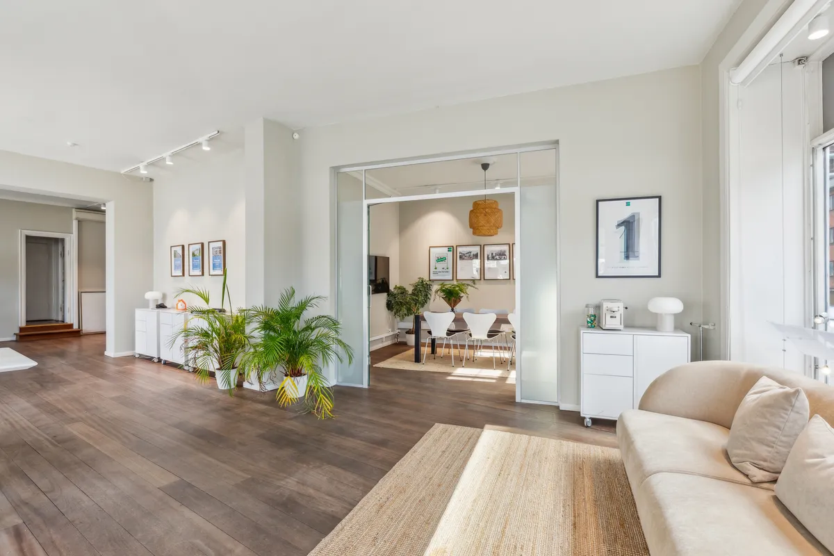 Et velmøbleret og moderne stue med højt til loftet, hvide vægge, lyse trægulve, store vinduer og indbydende møbler og