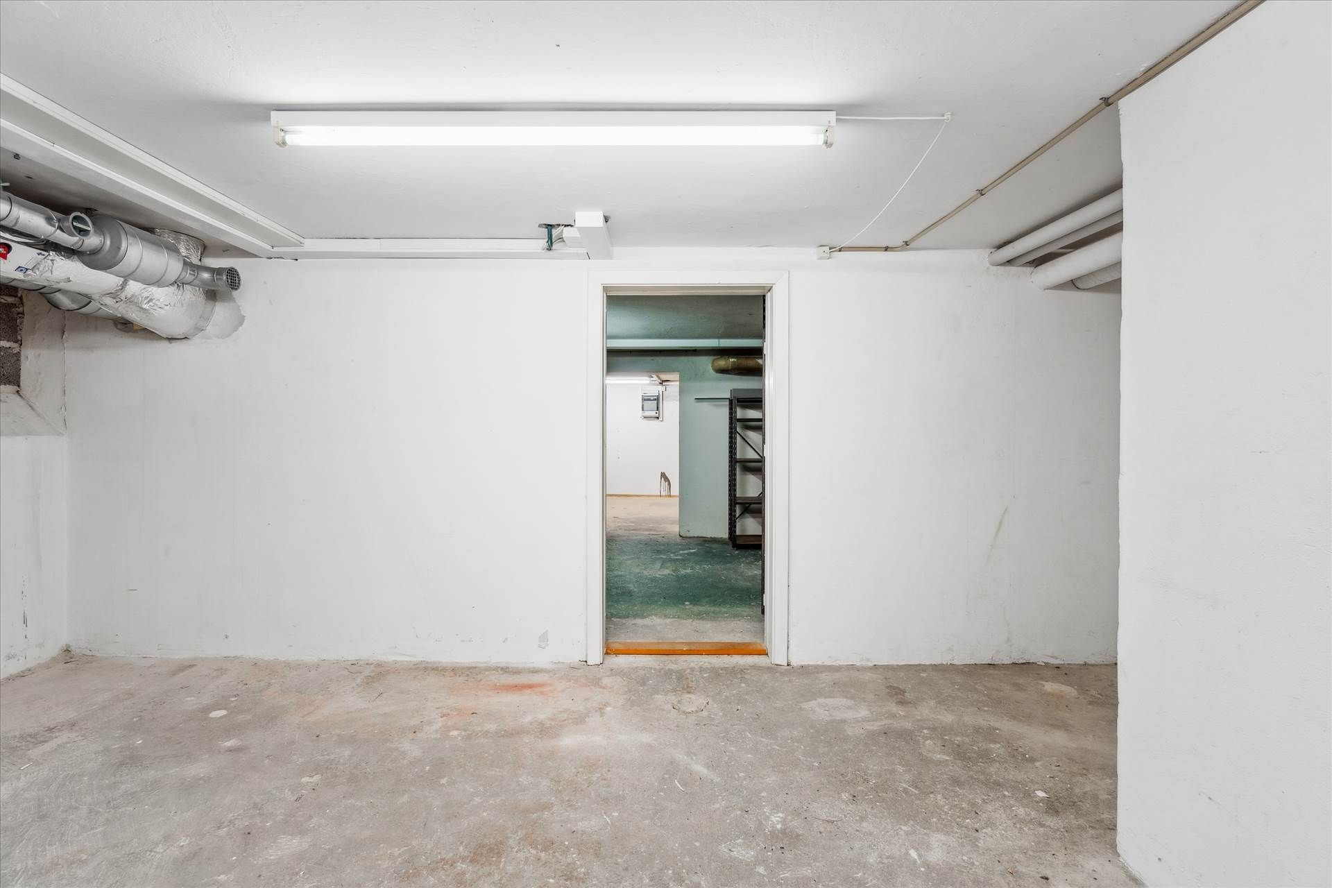En ren og tom underjordisk garage med hvide vægge og cementgulv samt lyse og røre på væggene og loftet