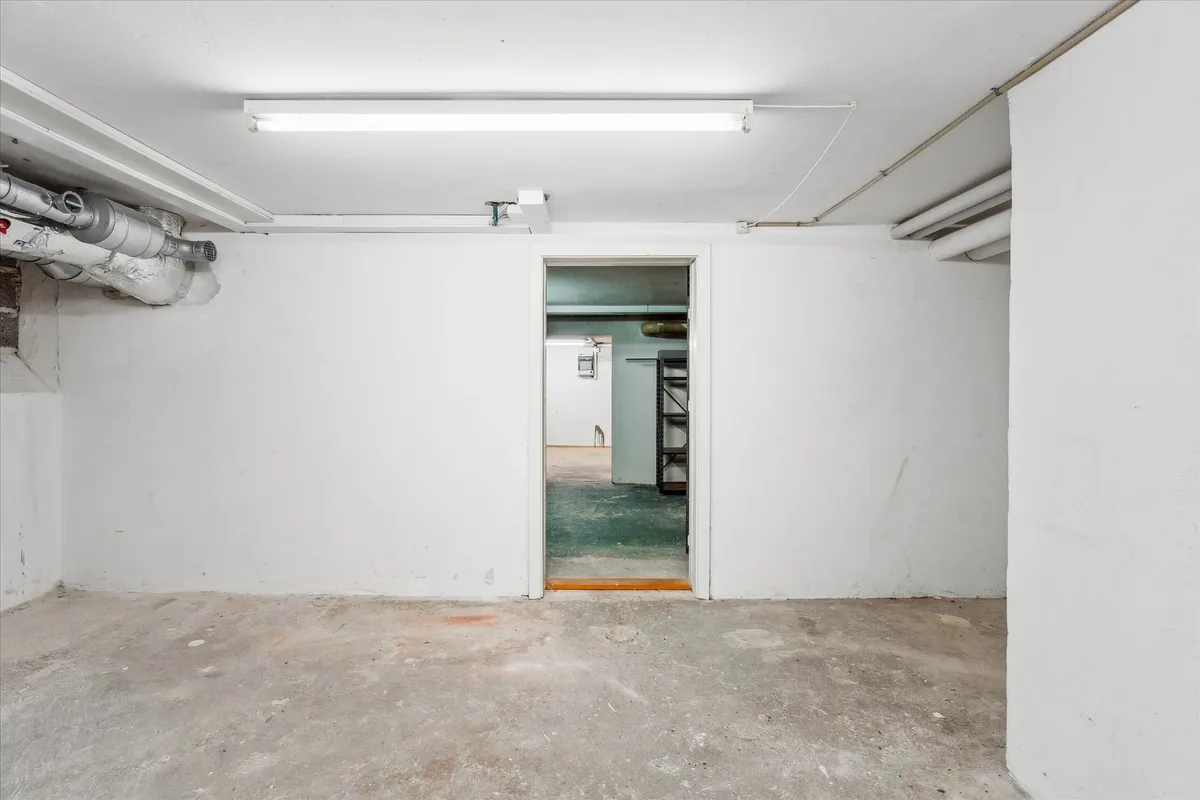 En ren og tom underjordisk garage med hvide vægge og cementgulv samt lyse og røre på væggene og loftet