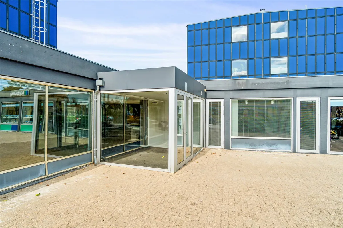 En glasdør fører ind i et erhvervslejemål med et glasadgangsparti og en lyseblå facade med mange vinduer