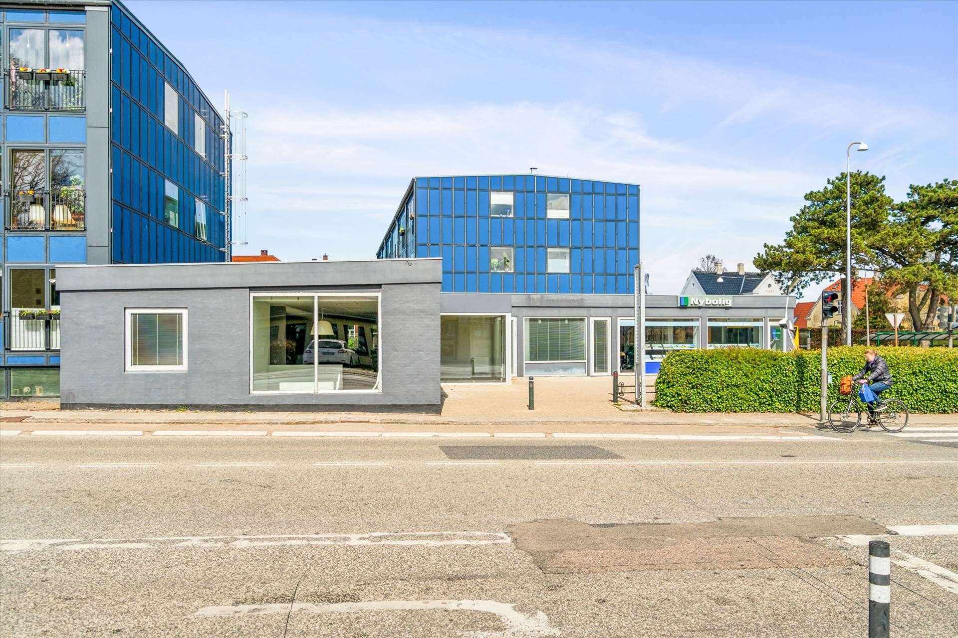 En cyklist kører på krydset i en fredelig by med nybolig i baggrunden, som er dækket af solpaneler, og et stort hus med blå