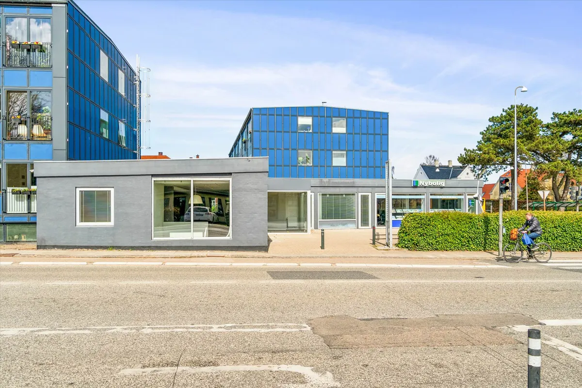 En cyklist kører på krydset i en fredelig by med nybolig i baggrunden, som er dækket af solpaneler, og et stort hus med blå