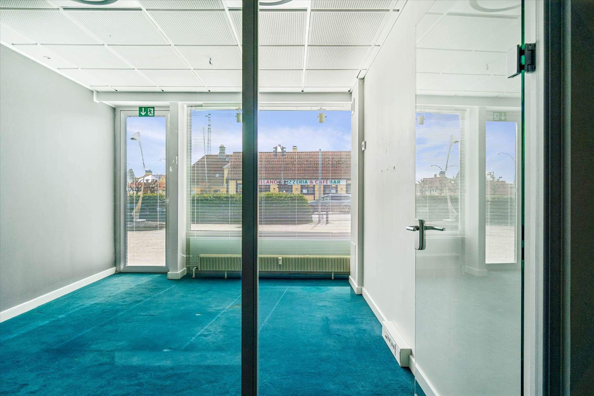 Et mødelokale med hvidt loft, vægge og gulv samt glasdøre og vinduer med rullegardiner