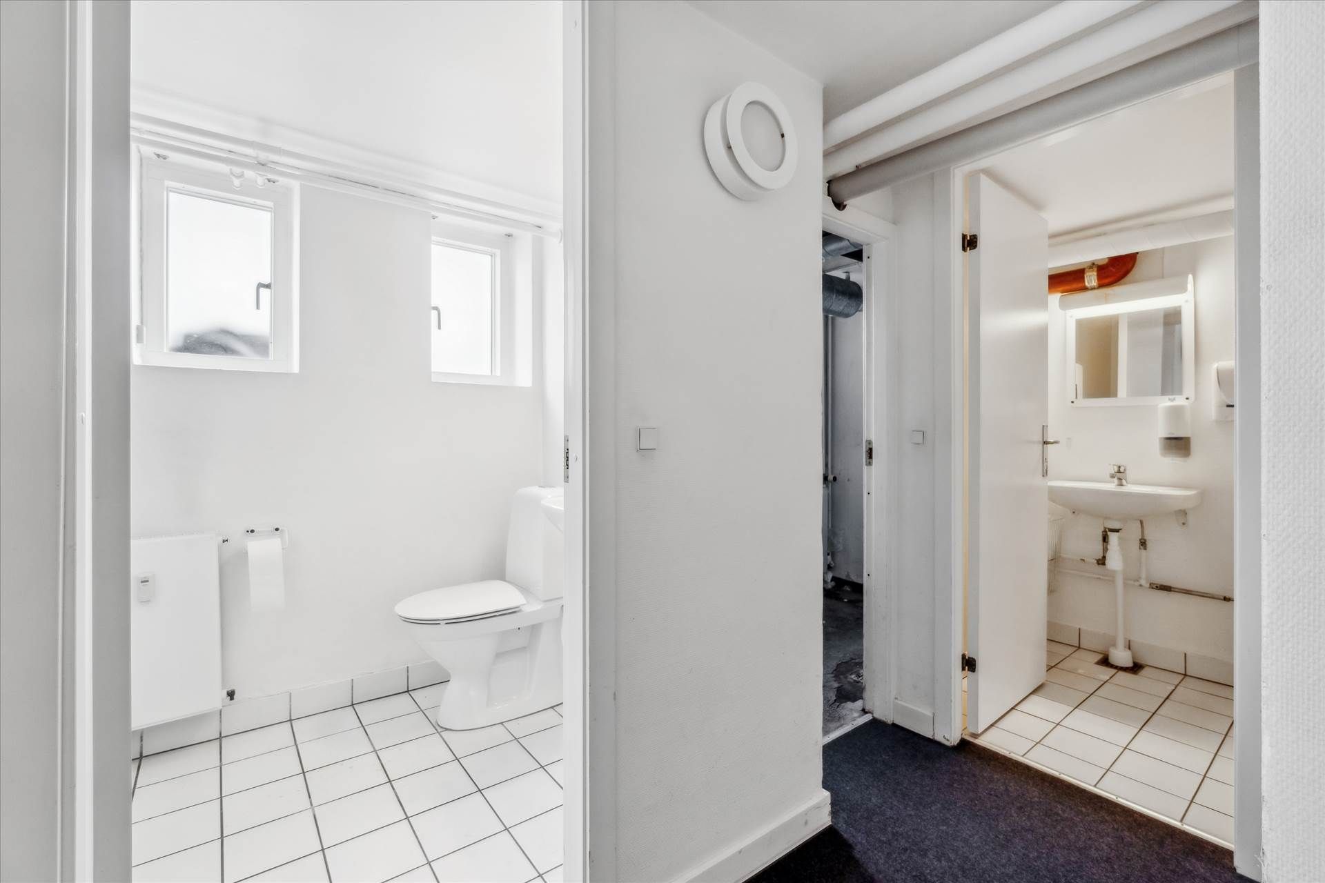 Ren og tørt badeværelse med hvidt toilet og hvidt gulv og vægge samt hvidt spejl og hvid vask med samme farve på gulv og