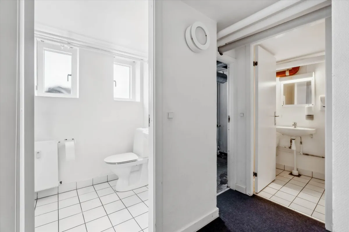 Ren og tørt badeværelse med hvidt toilet og hvidt gulv og vægge samt hvidt spejl og hvid vask med samme farve på gulv og