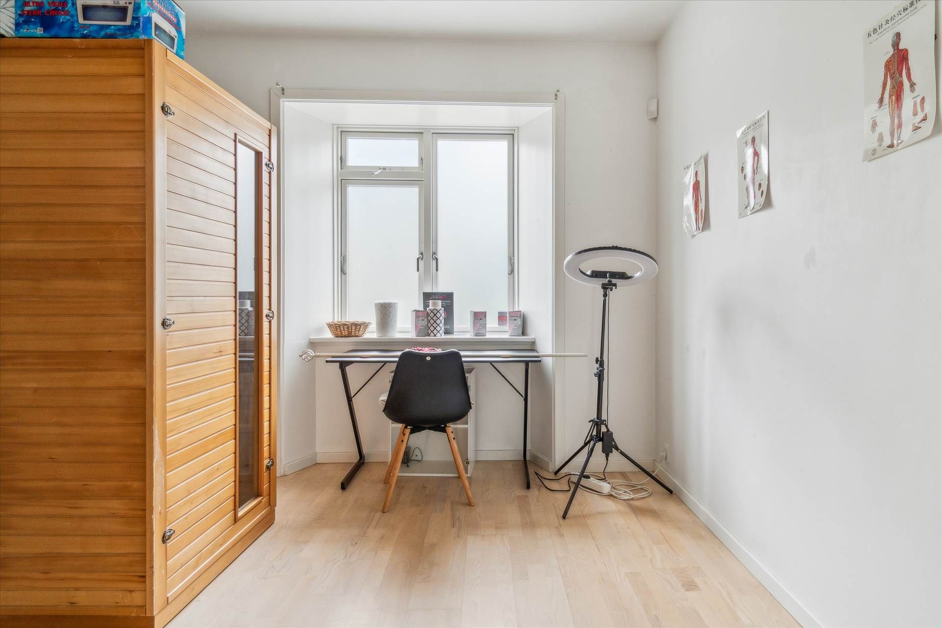 Studie med lysegul gulv og hvide vægge med et skrivebord og en stol samt en lampestativ og flere plakater