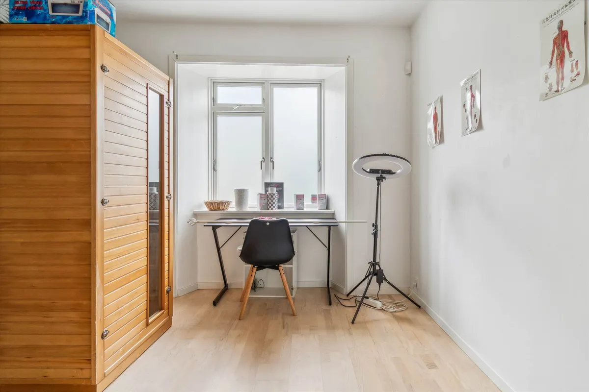 Studie med lysegul gulv og hvide vægge med et skrivebord og en stol samt en lampestativ og flere plakater