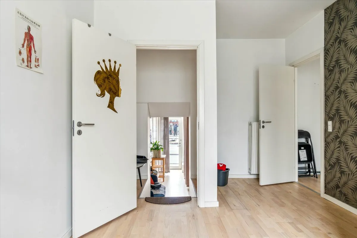 Butik med åben dør og lysegul gulvbelægning, tomme stolpe og væg med mønstret tapet