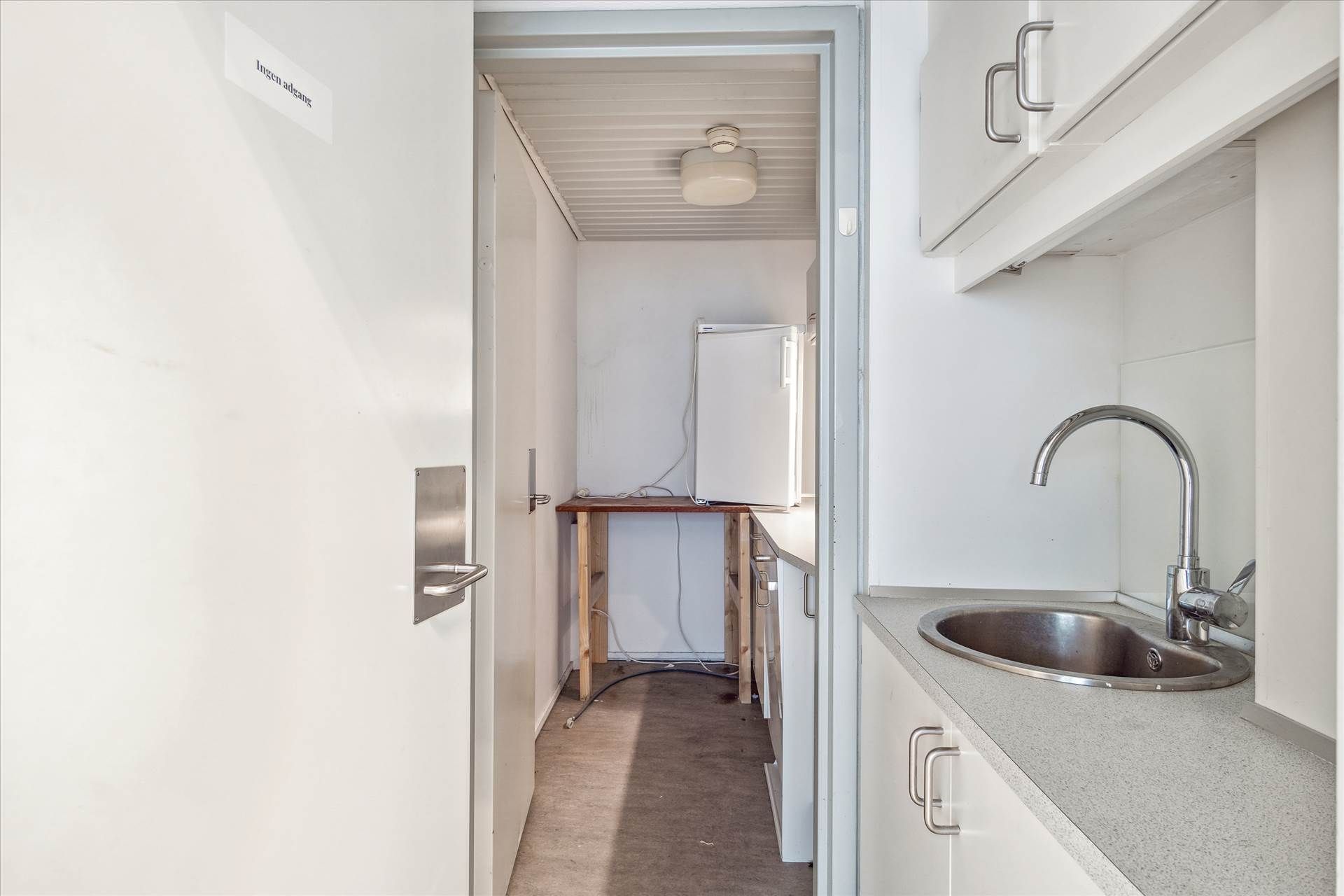 Lejlighed med åbent køkken, hvidt loft, understøtter og håndtag, lysekroner, træbord og køleskab, og en stor metalvandhane