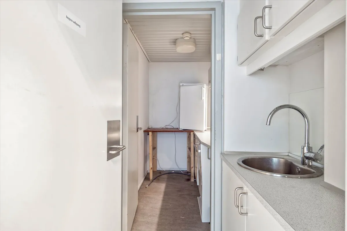 Lejlighed med åbent køkken, hvidt loft, understøtter og håndtag, lysekroner, træbord og køleskab, og en stor metalvandhane