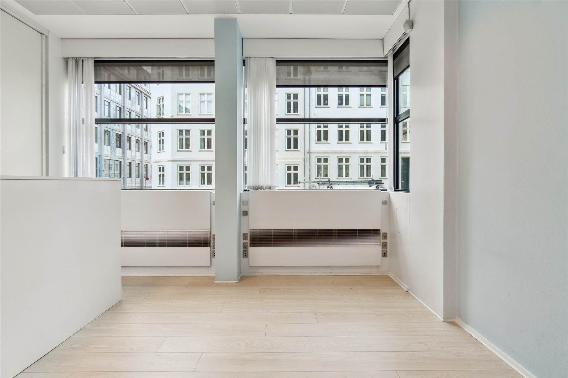 Moderne og minimalistisk indretning med hvide vægge og gulv samt store vinduer med udsigt til gaden og bygninger