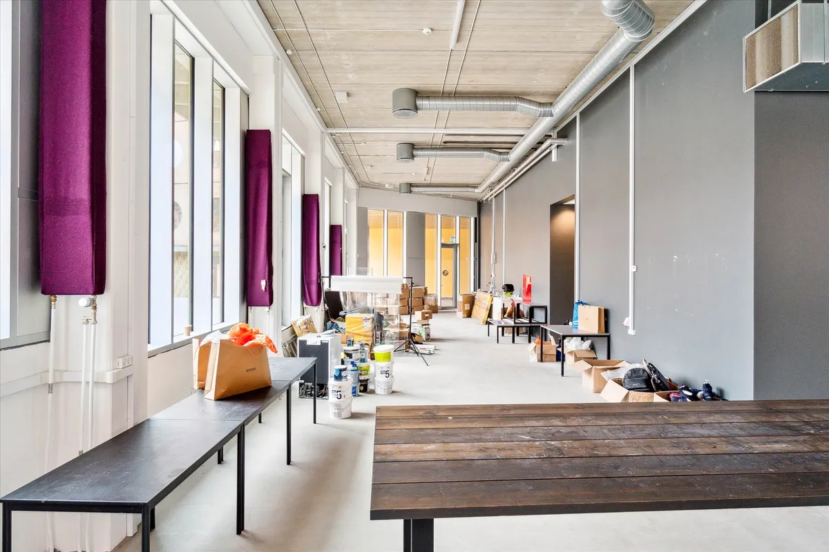 Kort og langt gang i lukket erhvervslokal med store vinduer og lyse lofter og gulv. Diverse kasse og vogne med materialer