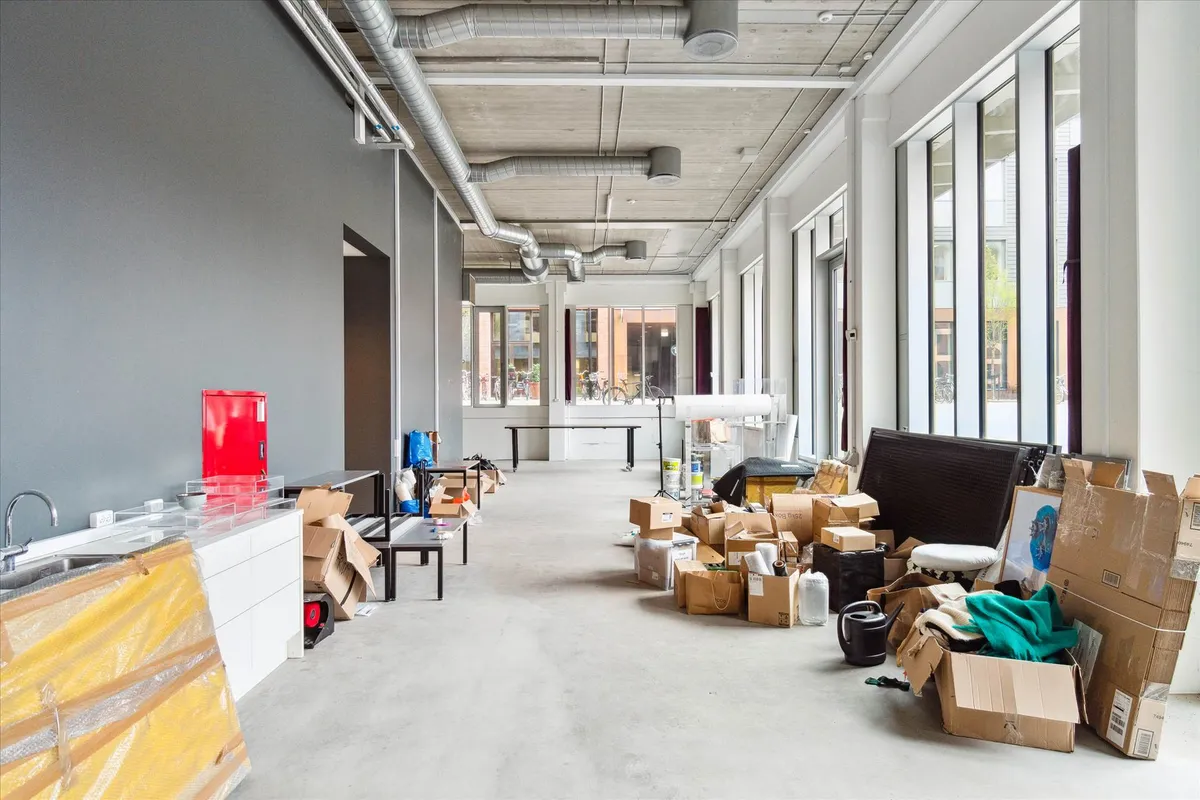 Et køkken med en række kasser, en væg med metalrør og mange vinduer med udsigt til udendørs cykler og planter