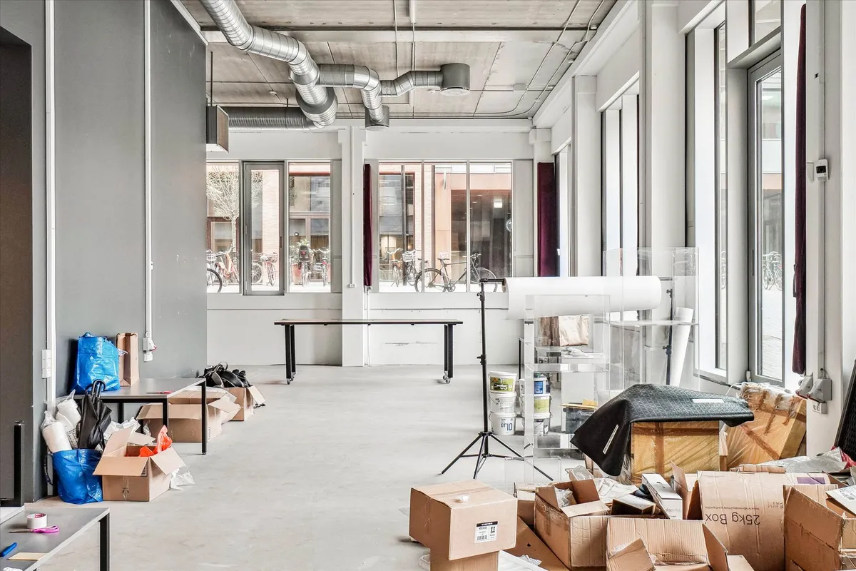 Stort rum med tømmer og stolpe, hvor der er flere kasser med tøj og poser samt en stativ med et glasvæg.