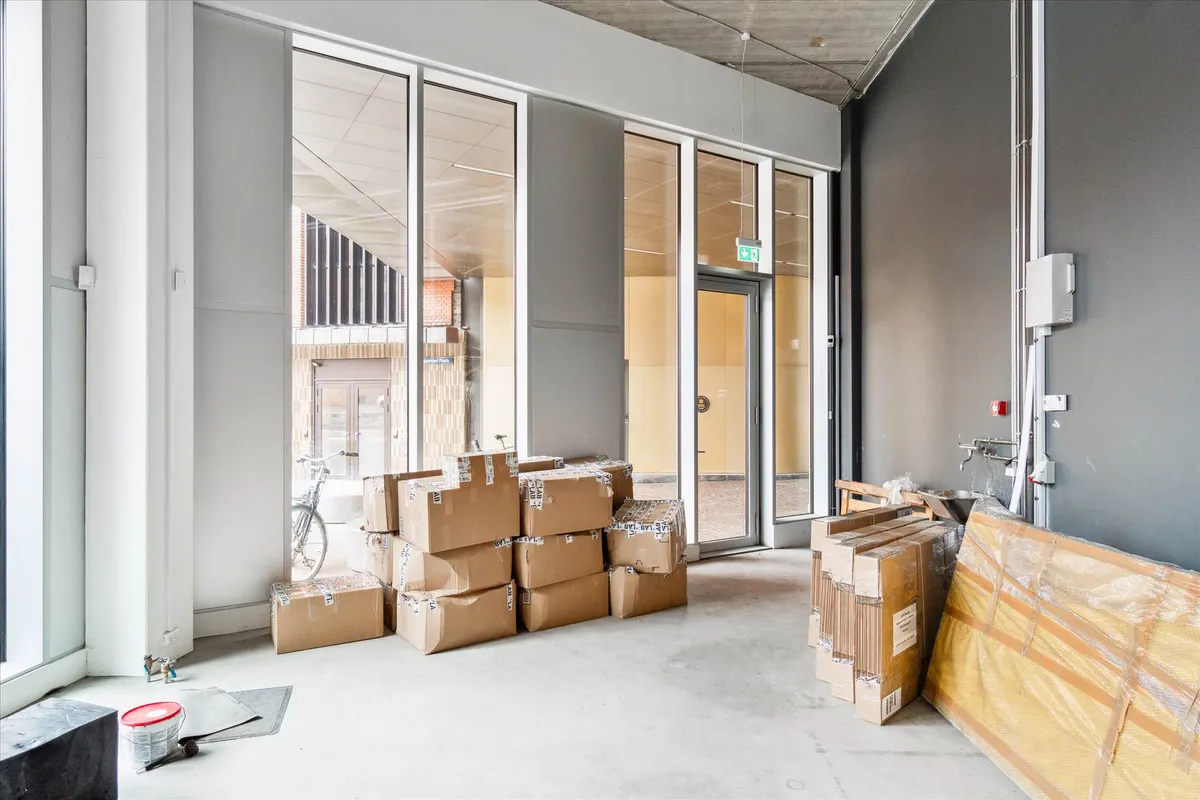 Byggepladsen med flere kartoner, måske under renovering, indeholder en stol og en cykel. Pladsen har høje vinduer og store