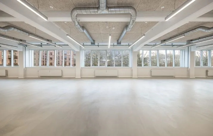 Rummelige kontorlokale med hvide vægge, lyse loftslampe, trægulv og store vinduer med udsigt til byen og træer