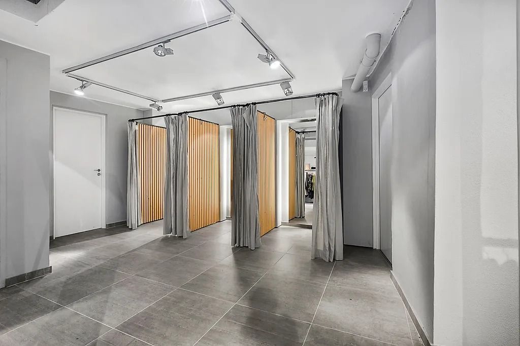 Et moderne og minimalistisk toiletrum med lysegule vægge, hvide døre og et gulv med store grå kvadratiske fliser samt lyse,