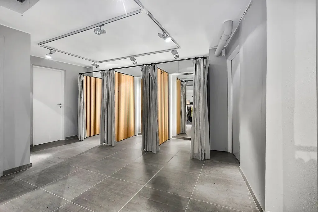 Et moderne og minimalistisk toiletrum med lysegule vægge, hvide døre og et gulv med store grå kvadratiske fliser samt lyse,