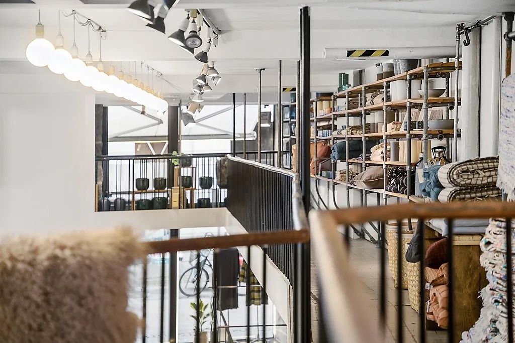 En stor indretning med møbler og hylder fyldt med tæpper, tøj og husholdningsgenstande, hvor lamper og lysekroner er ophængt