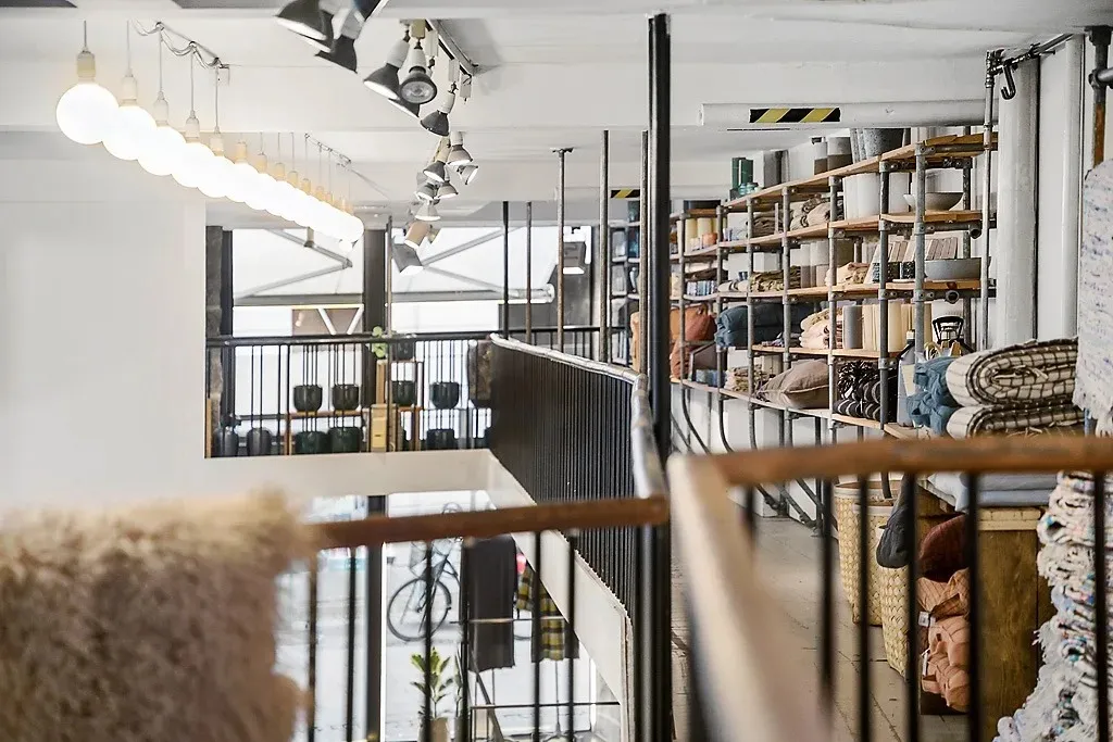 En stor indretning med møbler og hylder fyldt med tæpper, tøj og husholdningsgenstande, hvor lamper og lysekroner er ophængt