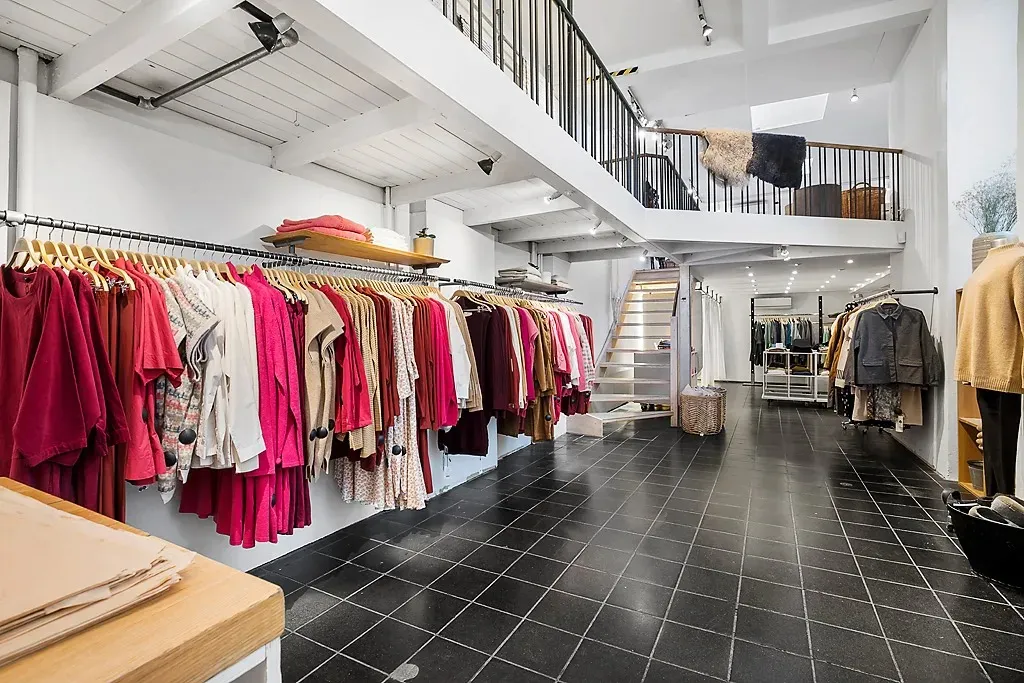 En klædeskab med tøj på hænge og ståhylder samt et trægulv og sort klinkegulv