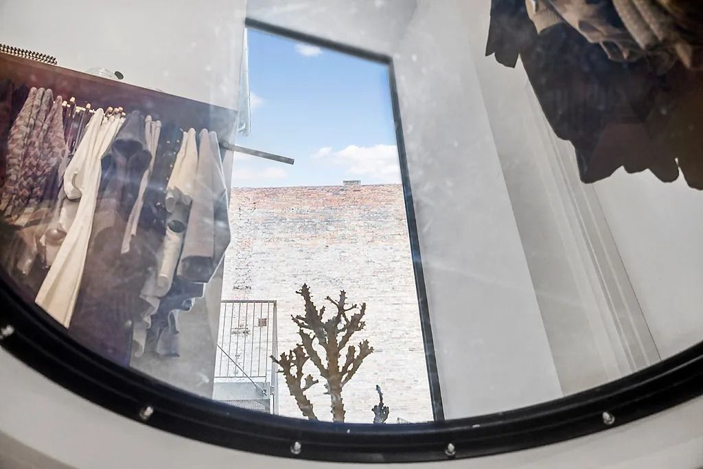 Rundt vindue viser indre med tøj og udsigt til bygning og træ